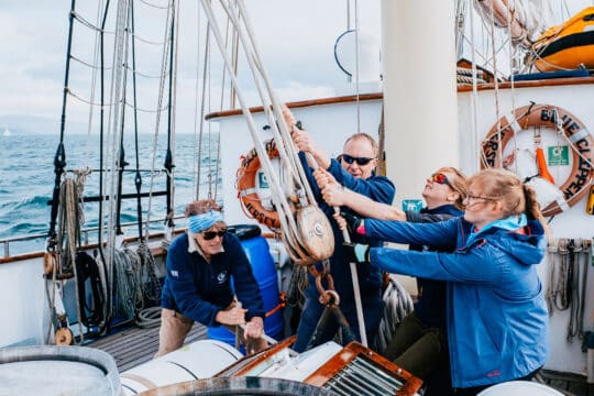 Blue Clipper guests raising sails pulling ropes