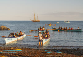 Bessie Ellen anchored off Cornish coast with gig racers on beach, Cornwall Isles of Scilly