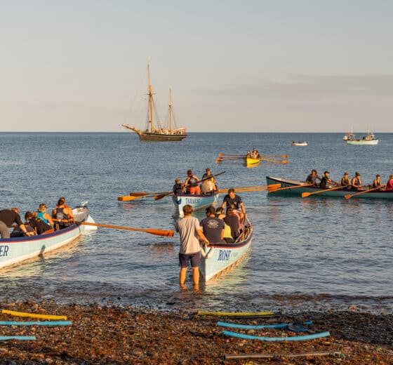 Bessie Ellen anchored off Cornish coast with gig racers on beach, Cornwall Isles of Scilly