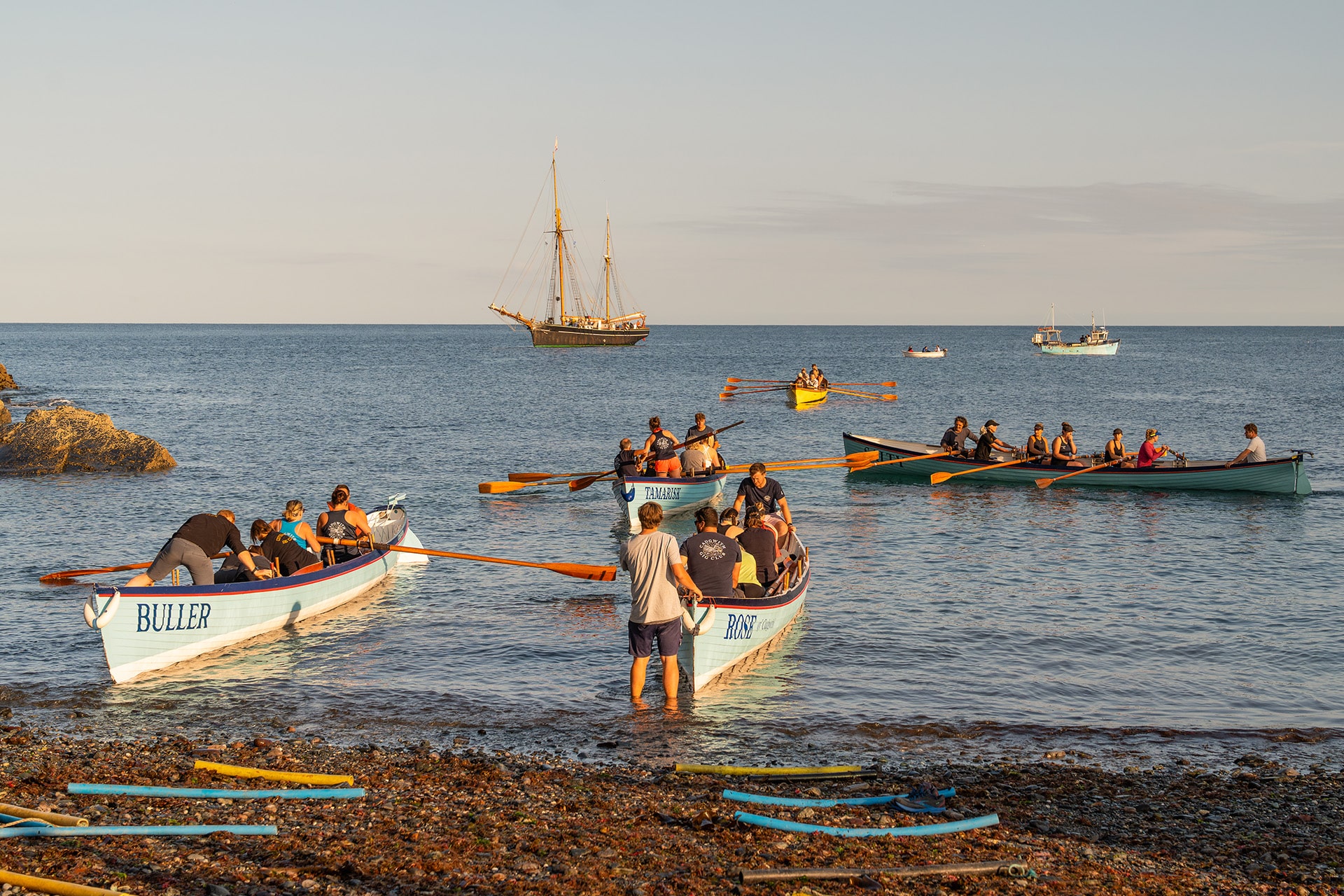 Bessie Ellen anchored off Cornish coast with gig racers on beach, Cornwall Isles of Scilly