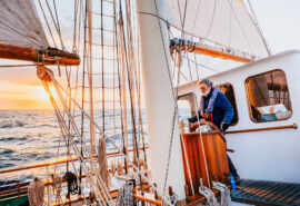 Blue Clipper guest at helm at sunset tall ship