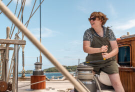 Chronos guest onboard working on the winches on deck female solo sailor