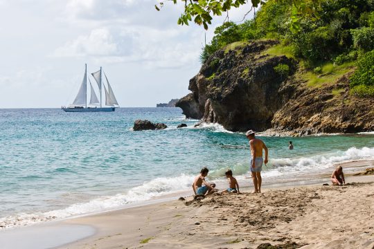 Family playing on Caribbean beach with Kairos sailing in background
