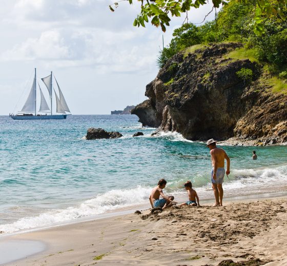 Family playing on Caribbean beach with Kairos sailing in background