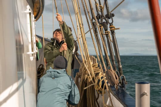 Flying Dutchman guests onboard raising the sails pulling ropes