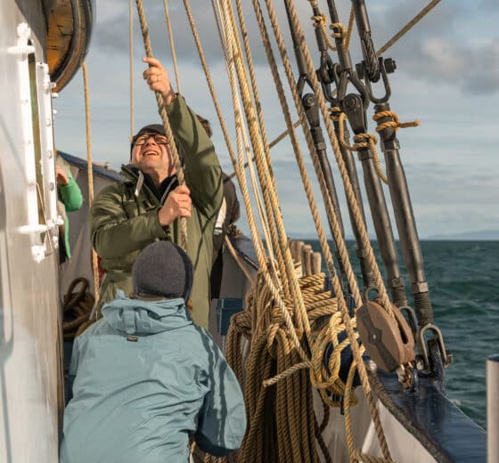 Flying Dutchman guests onboard raising the sails pulling ropes