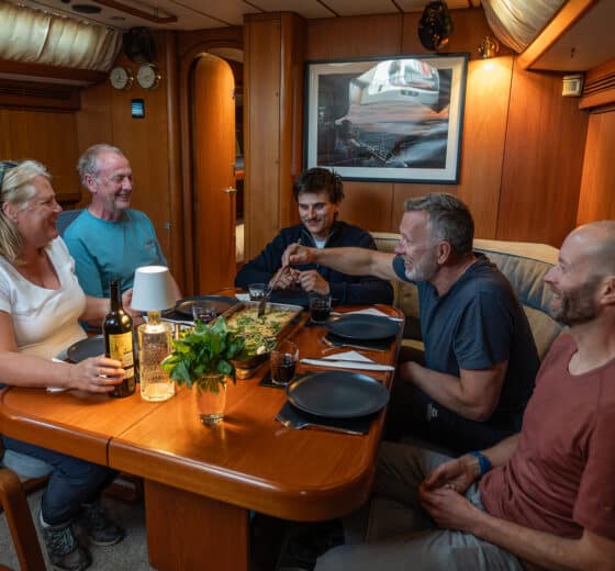 Noonmark VI adventure yacht below deck interior guests enjoying meal onboard dining dinner