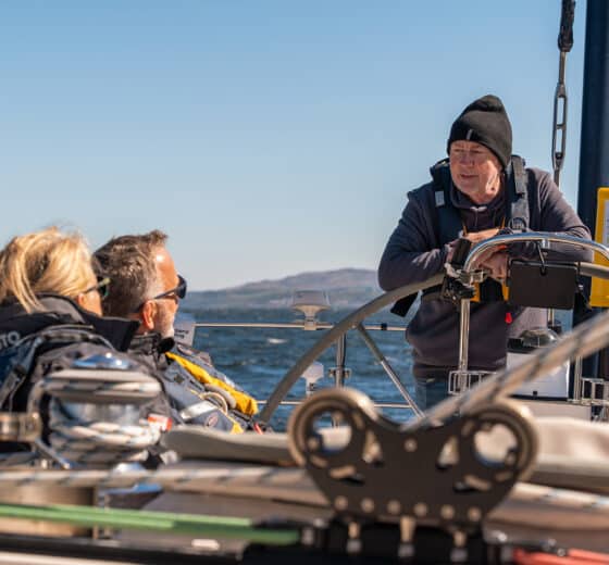 Noonmark VI guests with skipper at helm sailing in Scotland