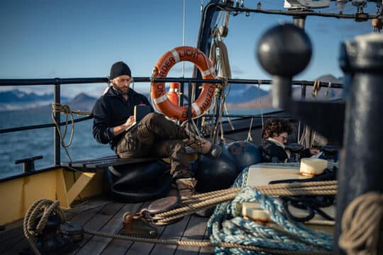 Noorderlicht tall ship guests relaxing reading on deck in Arctic Svalbard