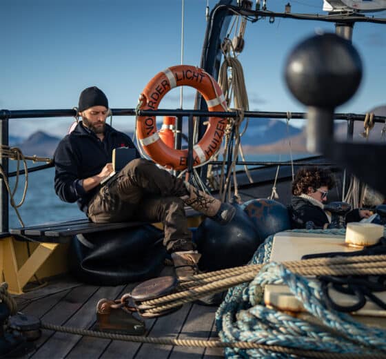 Noorderlicht tall ship guests relaxing reading on deck in Arctic Svalbard